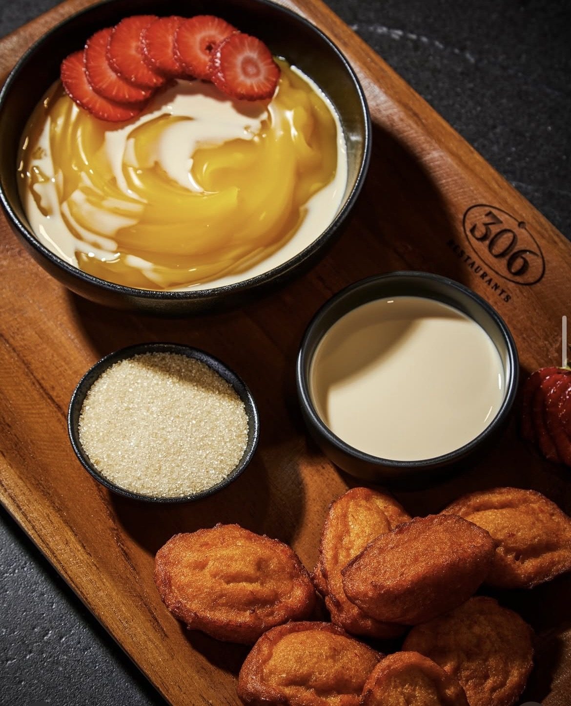 Warm sweet fritters served with custard, peak milk and strawberries